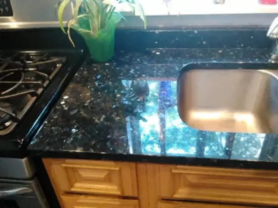 A black granite countertop with a sink, stove, wooden cabinets, and a green potted plant.