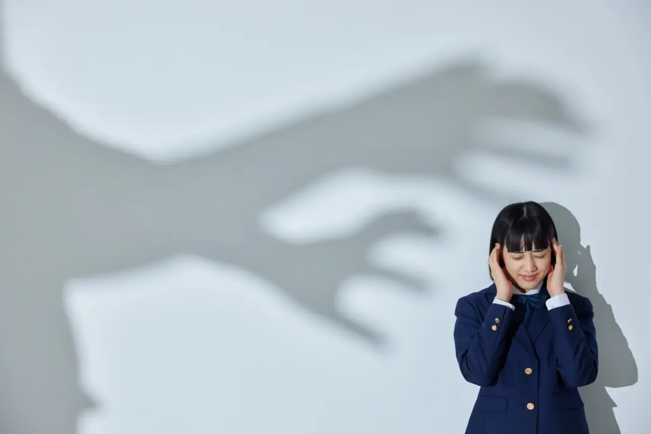 Girl covering ears stands near shadow of a large clawed hand reaching toward her on the wall.
