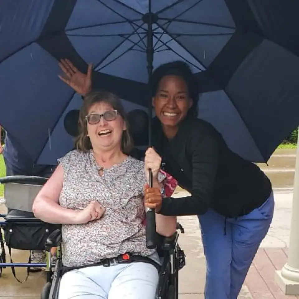 A registrant and a staff smile despite the rain, protected by an umbrella.