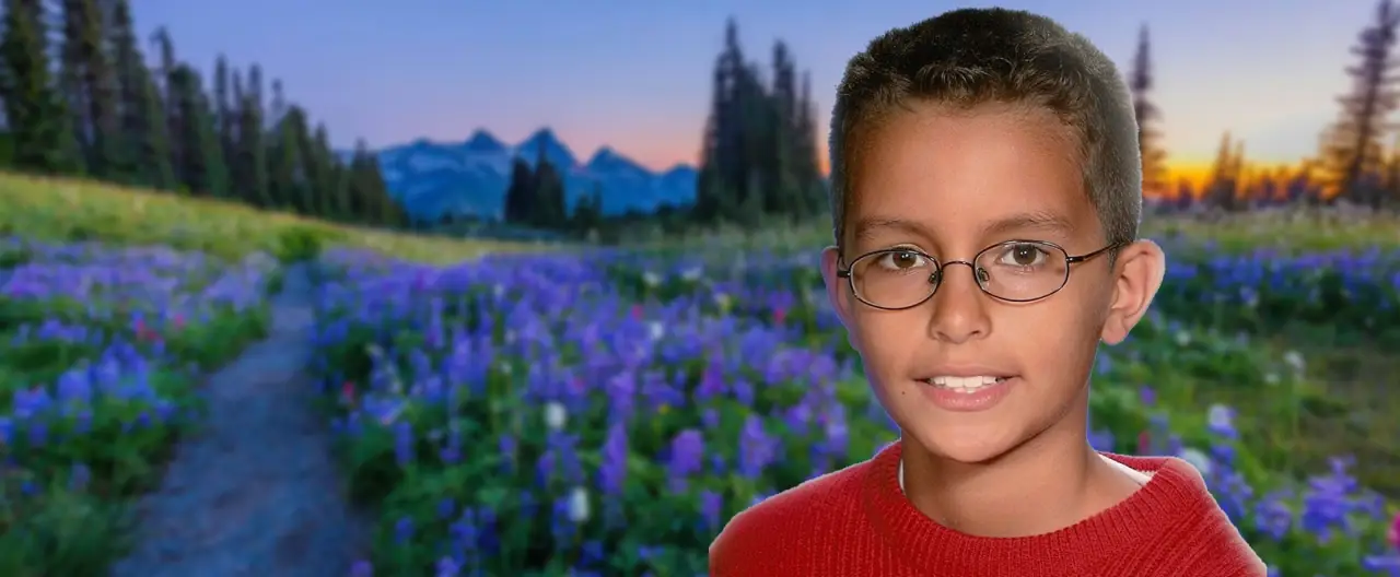 Joshua smiling before a mountain meadow filled with purple wildflowers.