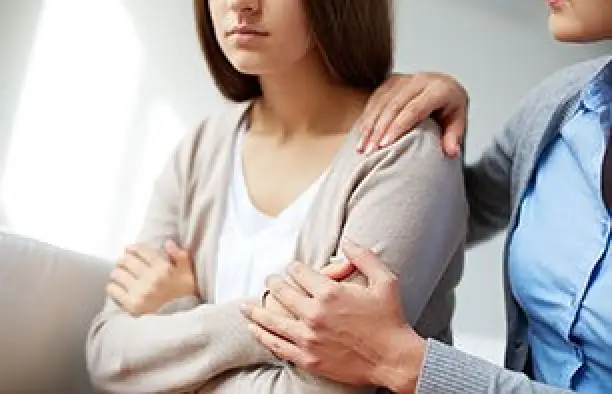 Two people sit close; one comforts the other by placing a hand on their shoulder and arm.