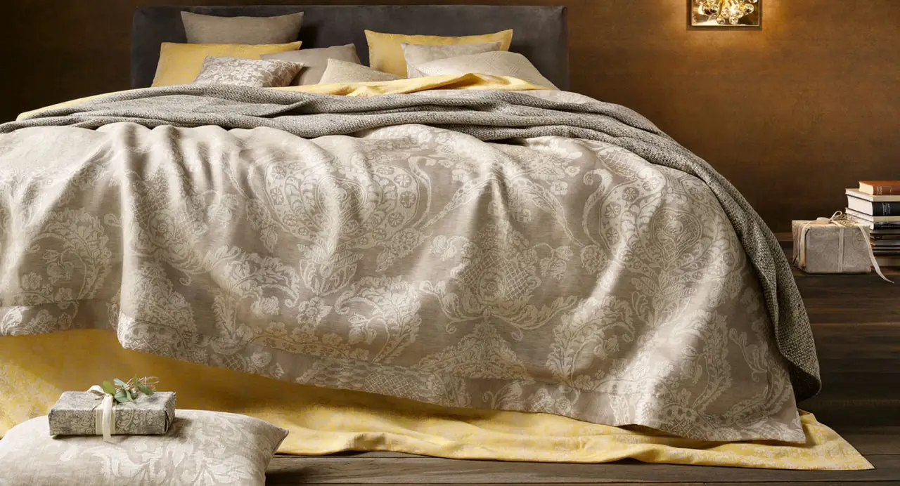 Bed with paisley duvet, gray throw, and yellow accent linens.