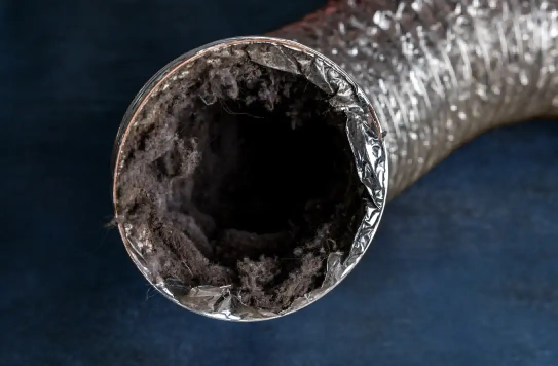 A dryer vent duct full of lint and dust against a dark blue background.