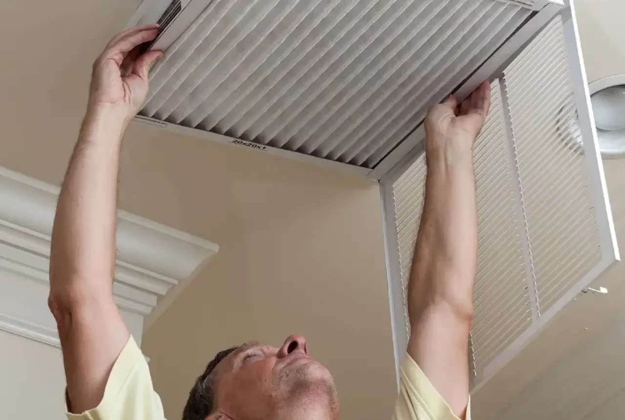 A person changes an air filter in a ceiling vent at home.