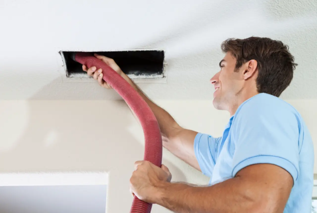 Technician cleaning a ceiling air duct with a red hose.