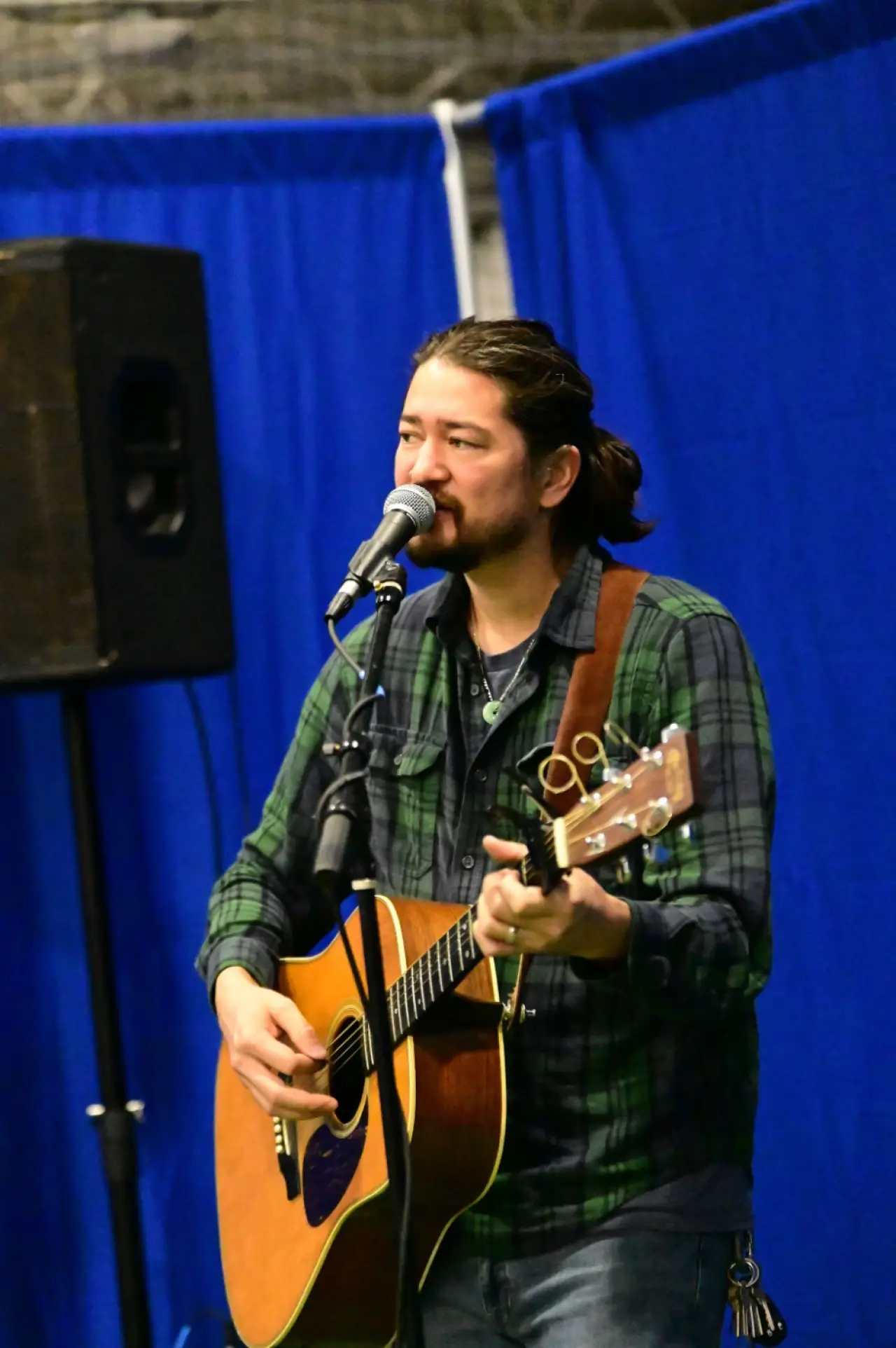 Musician sings into a microphone while playing guitar at the Ski Expo.