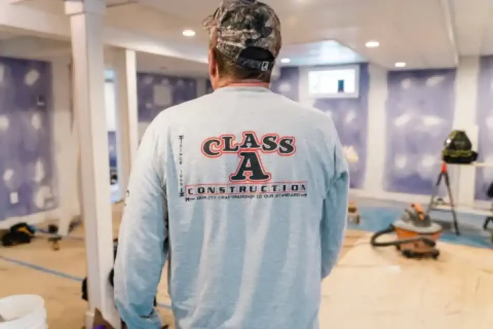 A man in a Class A Construction shirt stands in a room under renovation.