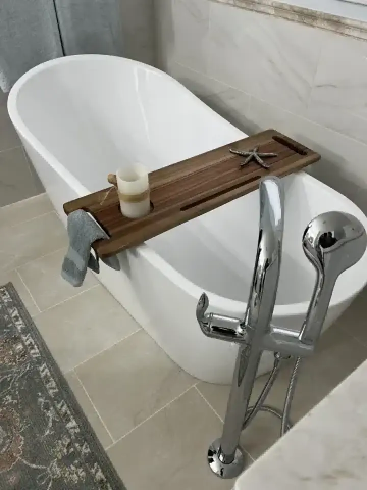 White bathtub with a wooden tray holding a candle and starfish, towel draped over the tray.