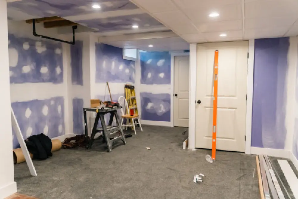 A room under renovation with drywall, tools, a ladder, and unfinished walls and ceiling.