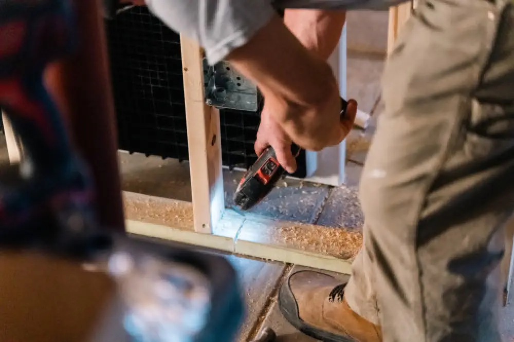 Person using a power drill on wood while constructing or renovating a building frame.