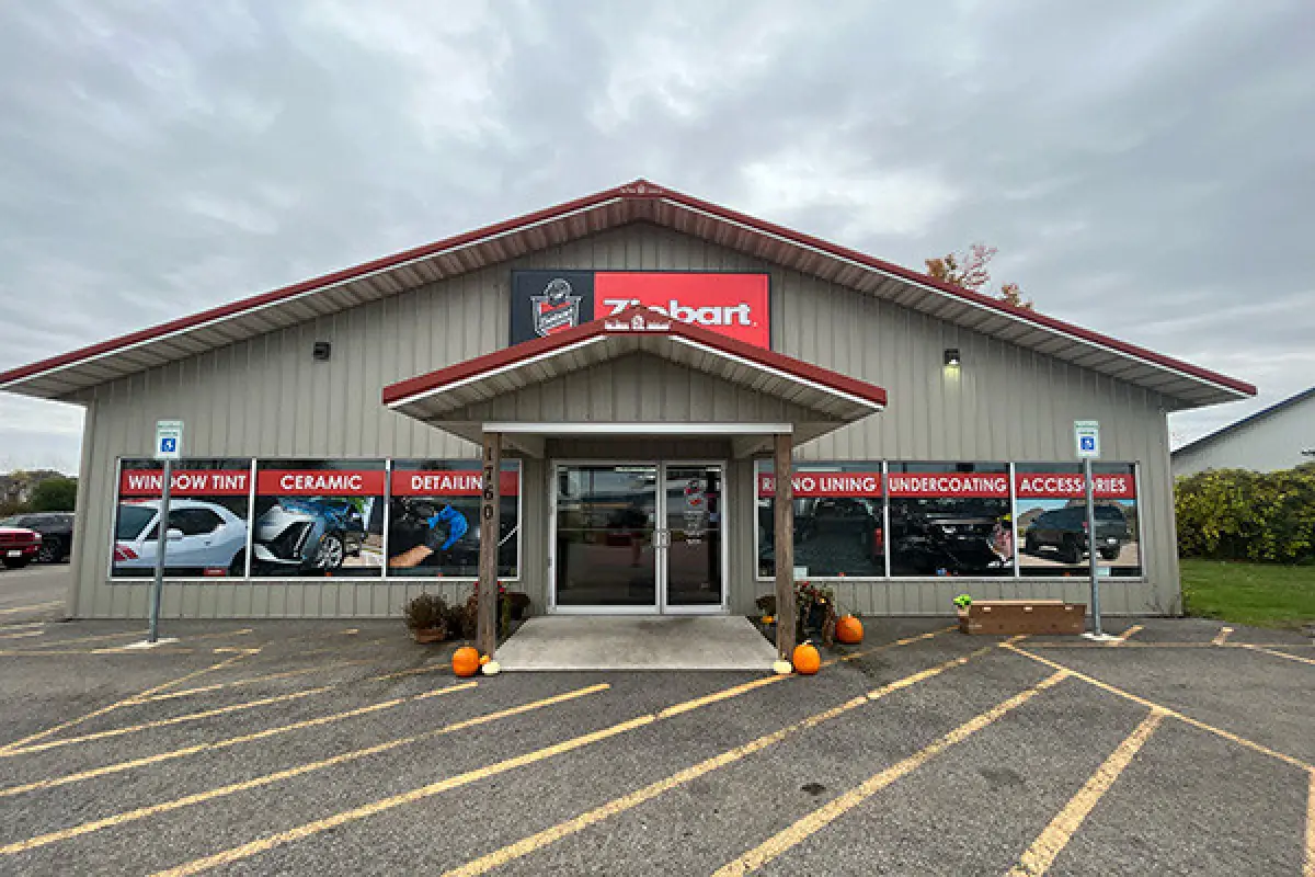 Storefront with red roof, signage for car services, and pumpkins at the entrance.