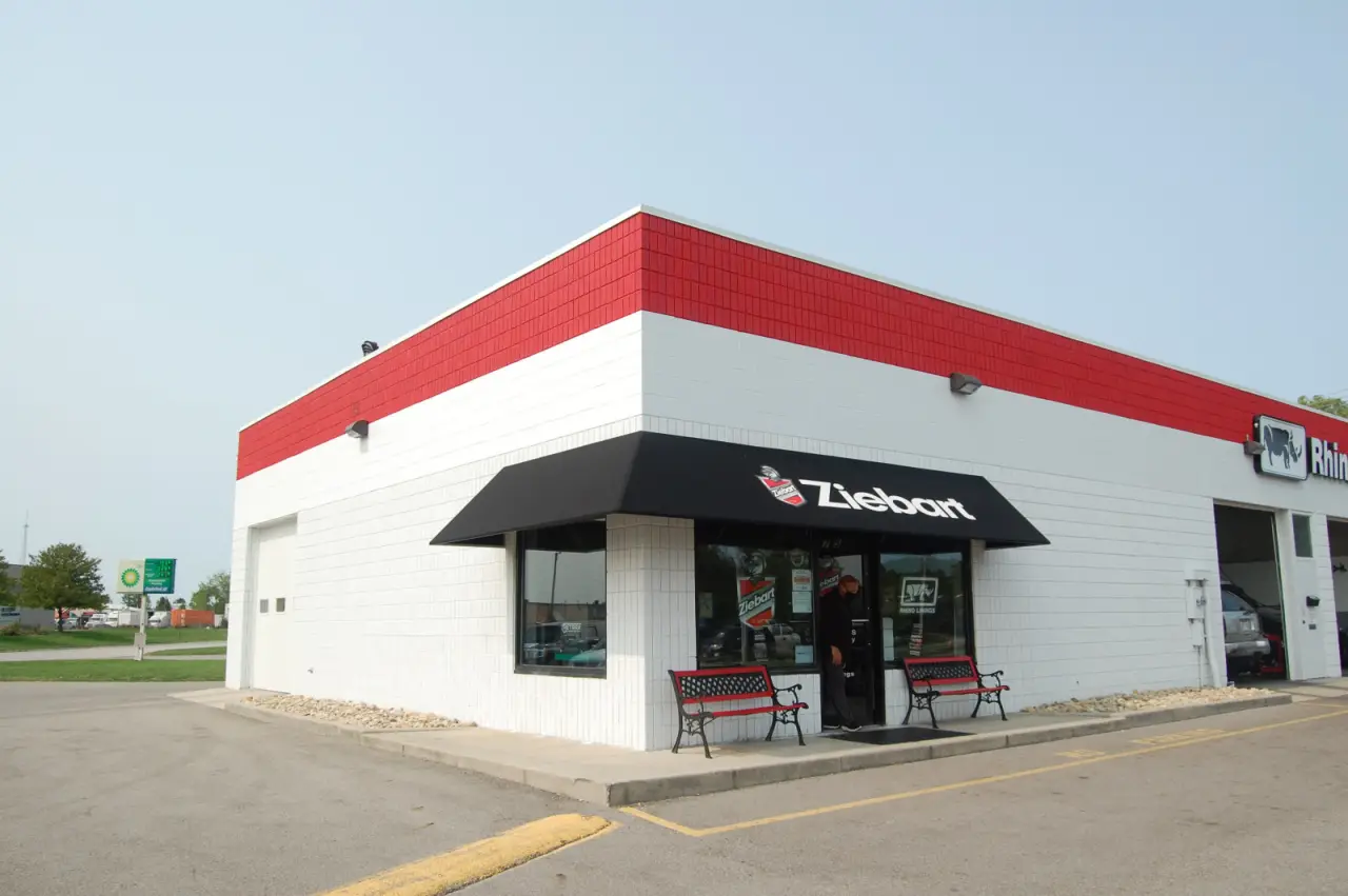 Exterior of a Ziebart shop with a black awning and two benches outside.
