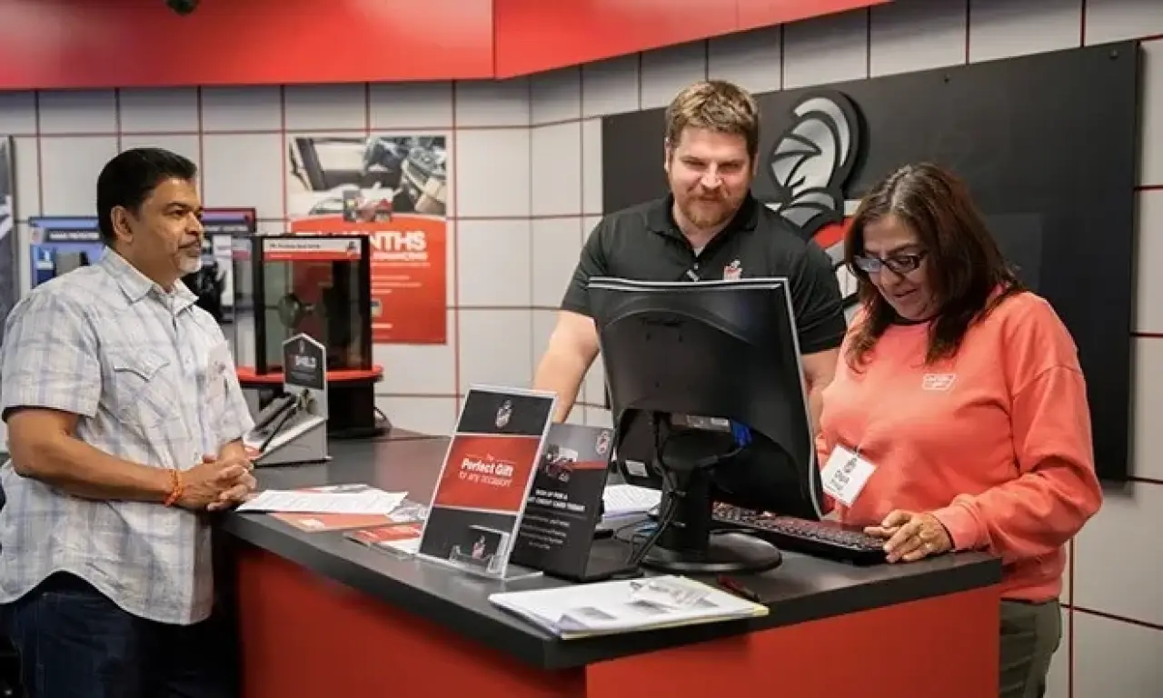 Three people stand at a service counter, discussing paperwork in an automotive shop setting.