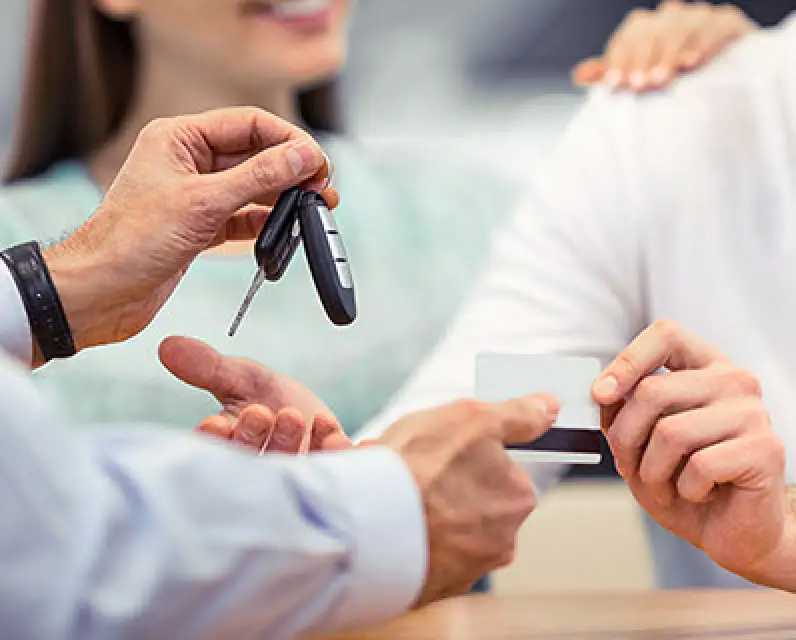 Person hands over car keys while another holds a credit card, with a woman smiling nearby.
