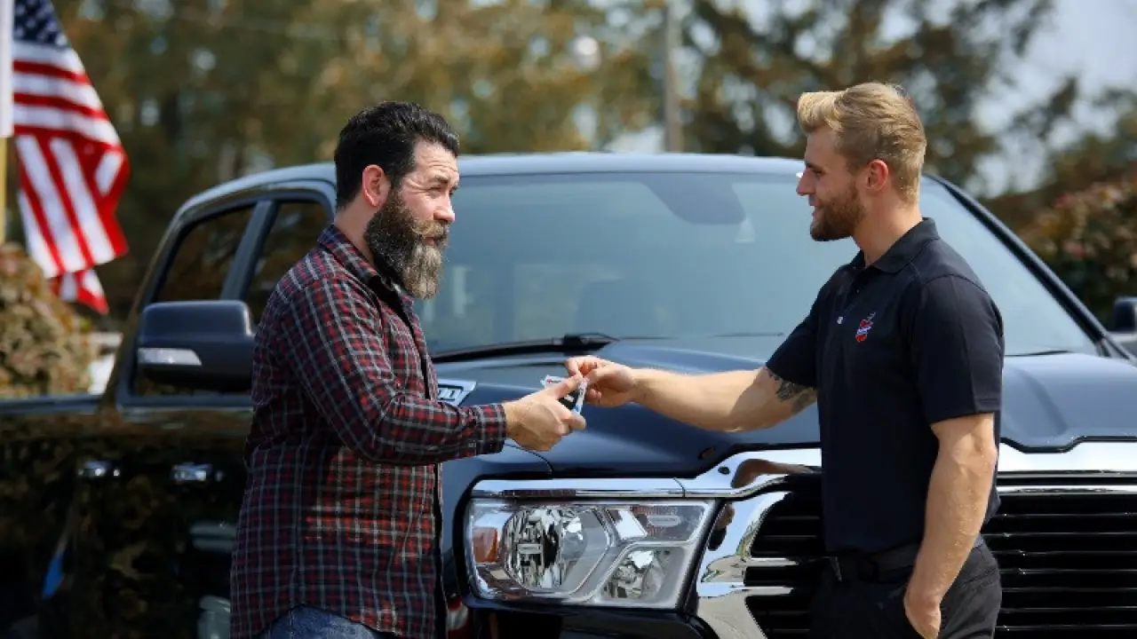 A man receives car keys from a dealership employee in front of a black pickup truck.