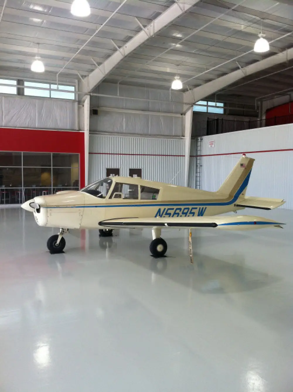 A small cream-colored airplane with blue accents sits inside a clean, bright hangar.