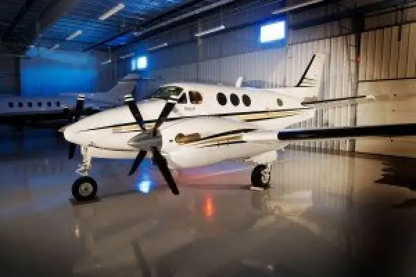 A small twin-propeller airplane parked inside a brightly lit aircraft hangar.