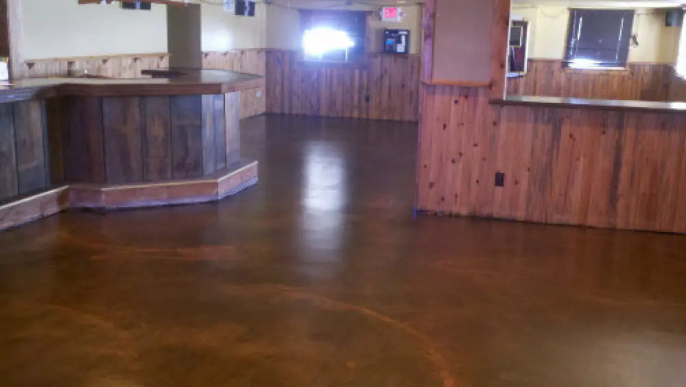 An empty room with polished brown floors and wood-paneled walls, featuring two counters.