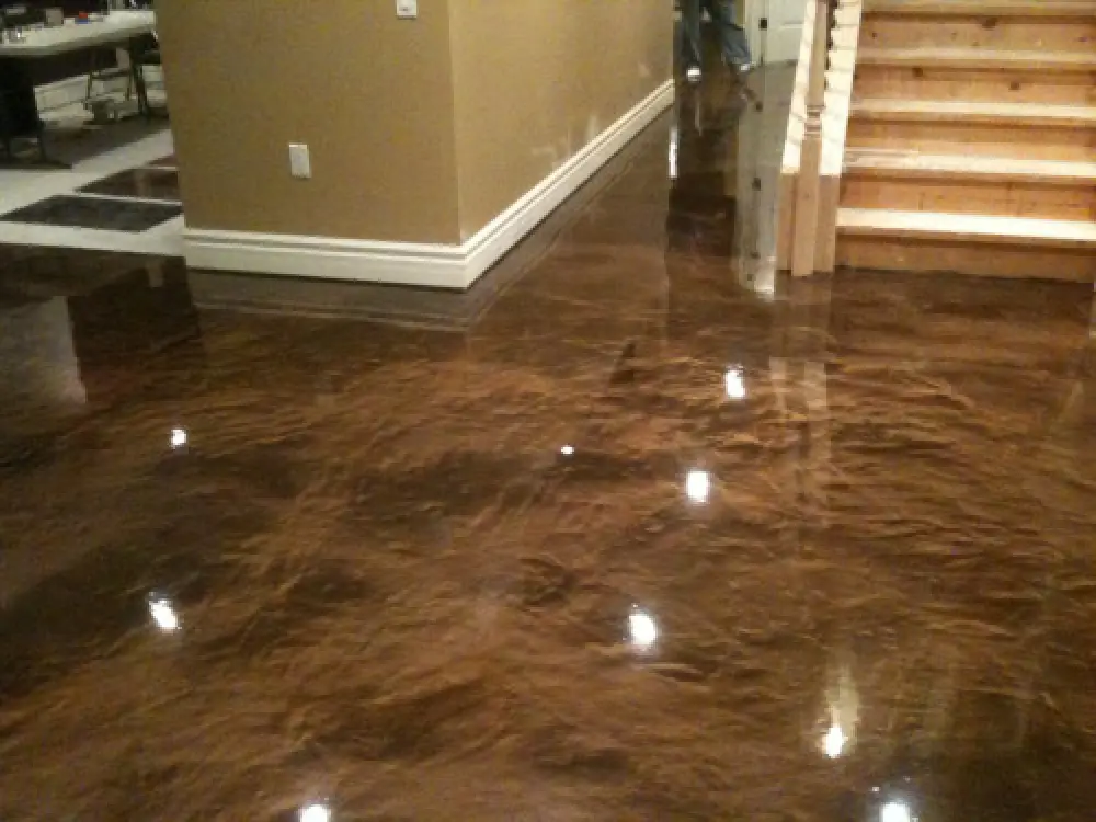 Glossy brown epoxy floor reflecting lights by wooden stairs and beige walls in a modern interior.