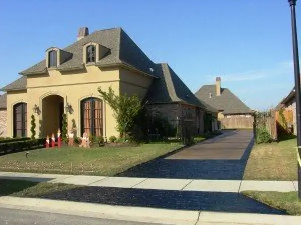 Cream-colored house with steep roof, wide driveway, and small lawn decorations in front yard.
