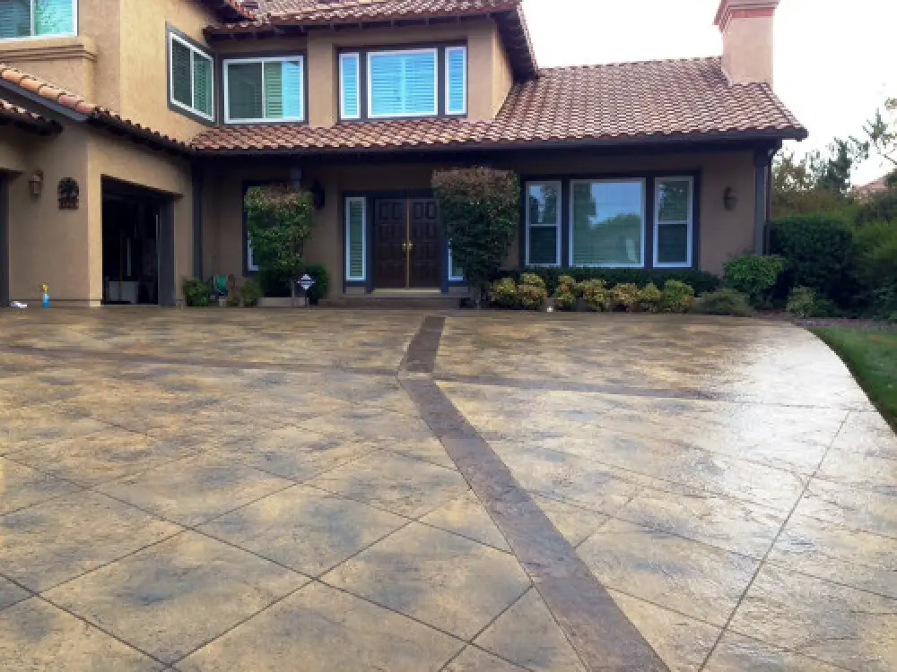Large tan house with tile roof and a patterned, stamped concrete driveway in the foreground.