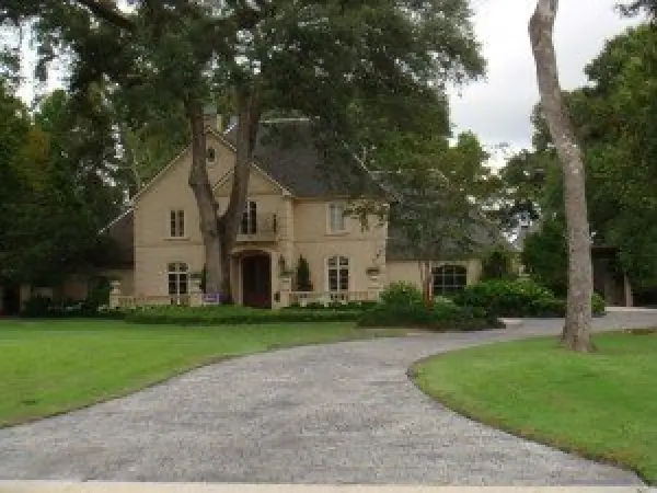 Large beige house with arched windows, surrounded by trees and a curved driveway in front.