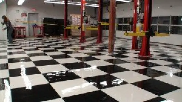 Auto shop with black and white checkered floor, car lifts, and a person in the background.