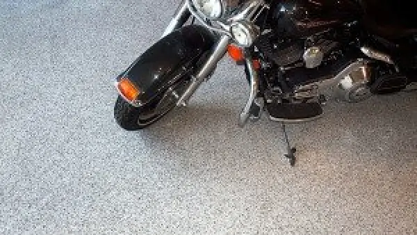 Black motorcycle parked on a speckled, light gray garage floor with its kickstand down.