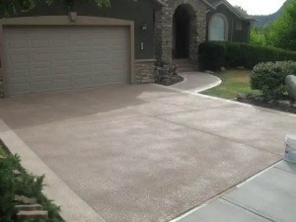 A clean, brown concrete driveway in front of a house with a stone-accented entryway.