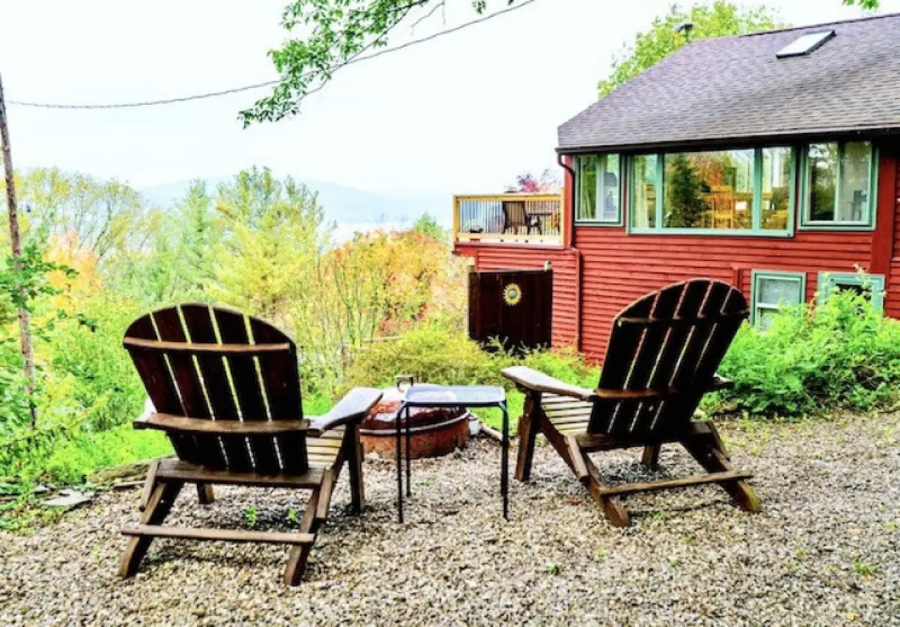 two wooden chairs overlook a scenic view near a red cottage with a fire pit in the foreground