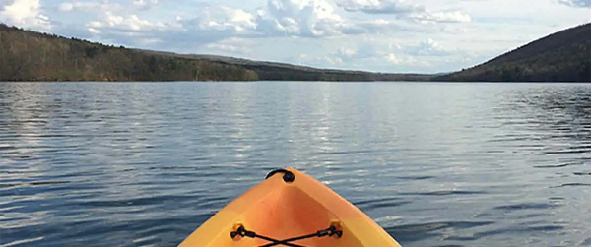 view from a yellow kayak gliding across a calm lake, surrounded by tree-covered hills