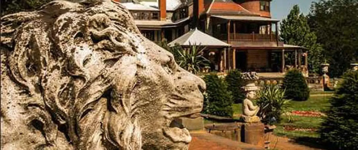 a stone lion statue in front of a large, historic house with lush greenery and gardens