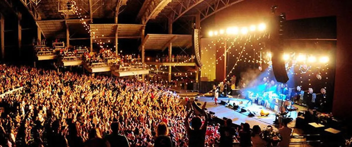 large crowd cheering at an indoor concert with bright stage lights and performers on stage