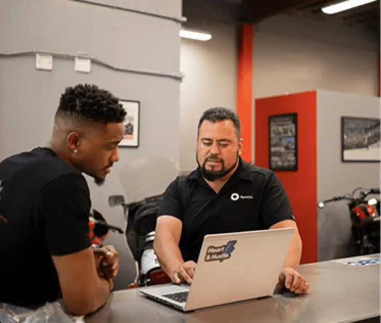 two men review analytics on laptop screen at a gray and red office space