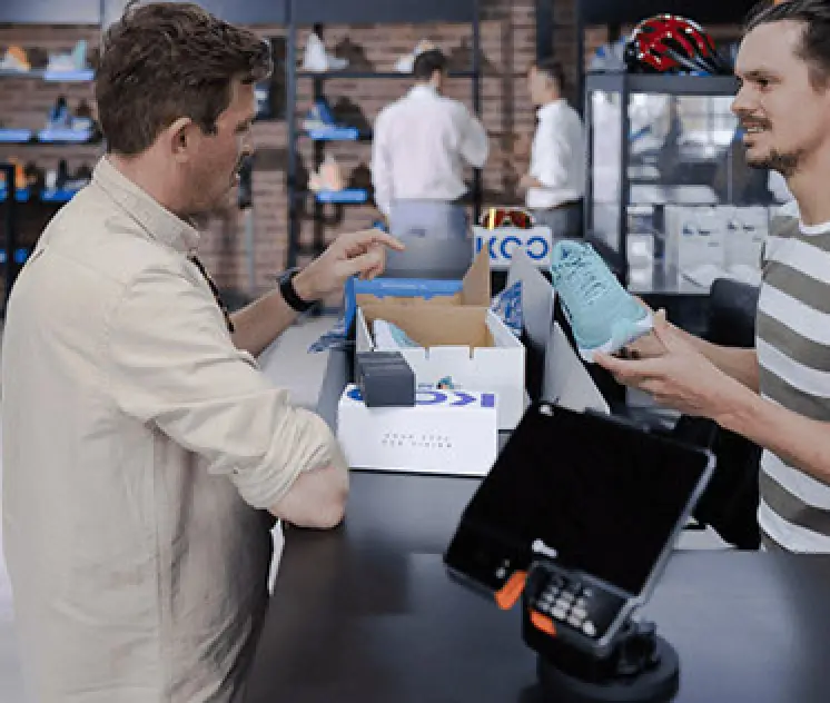 man in striped shirt at checkout counter holding blue sneakers speaking to customer