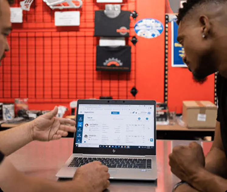 two men staring at computer screen reviewing metrics at merch shop