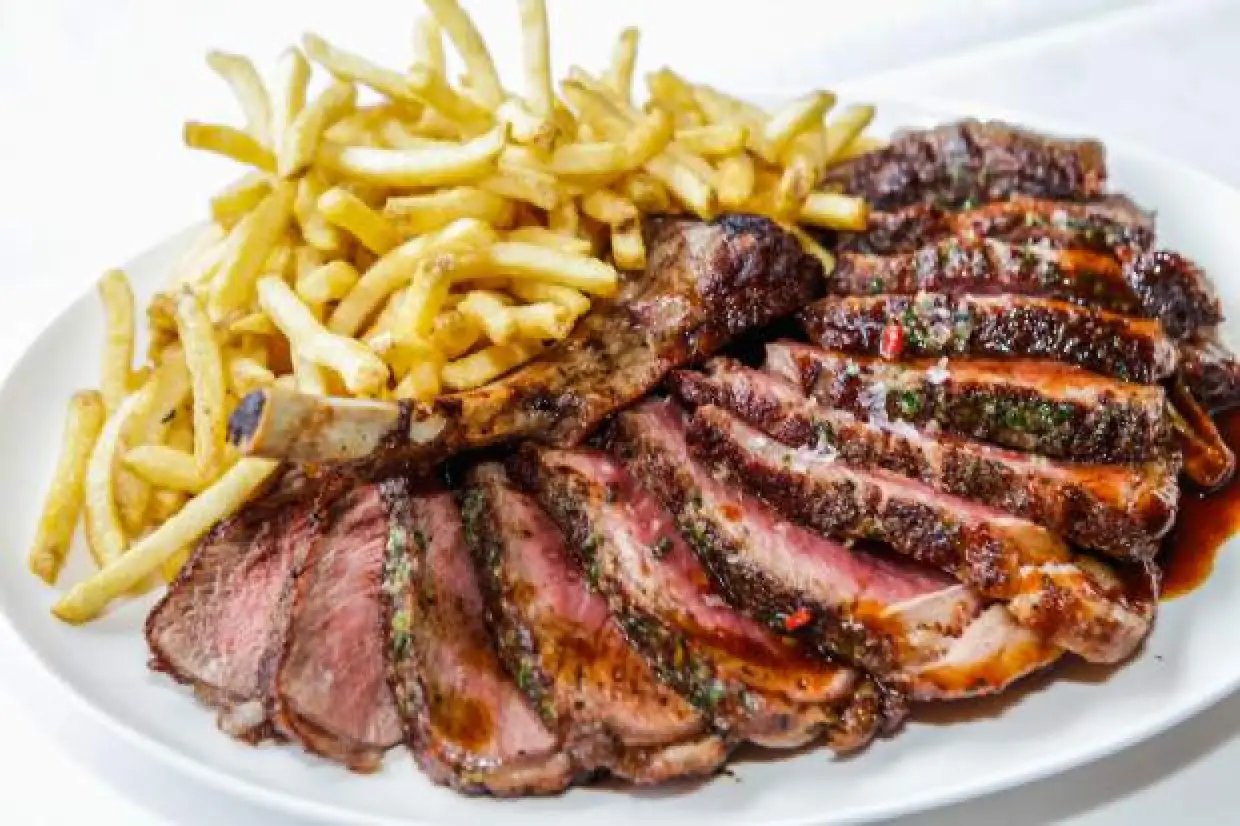 Sliced dry-aged steak with sauce and fries on a white plate.