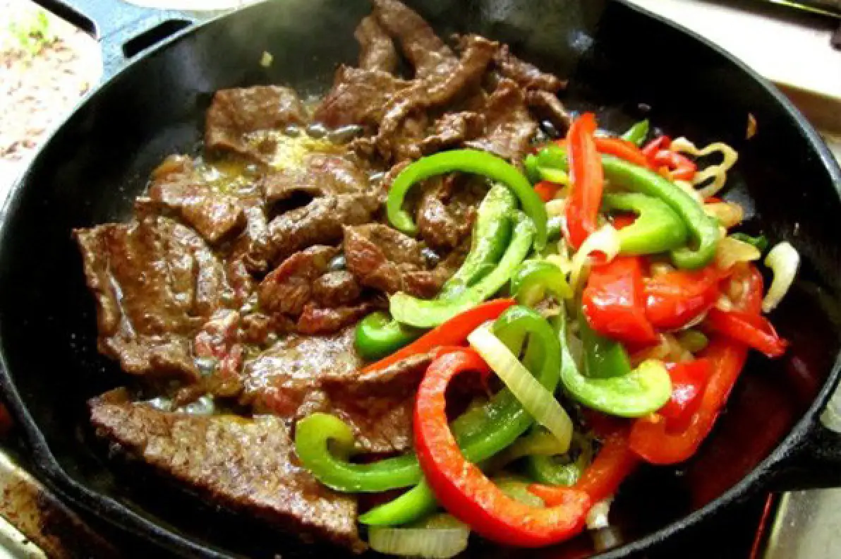 Pepper steak with bell peppers and onions cooking in a skillet.
