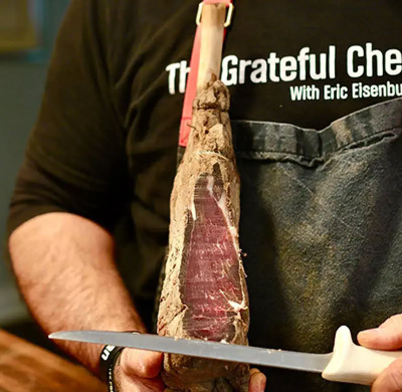 Chef trimming dry-aged beef with a long knife.