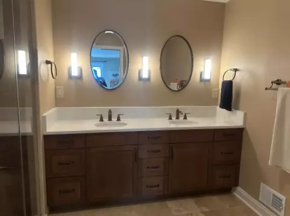 Bathroom with double vanity, oval mirrors, and wall lights above wooden cabinets.