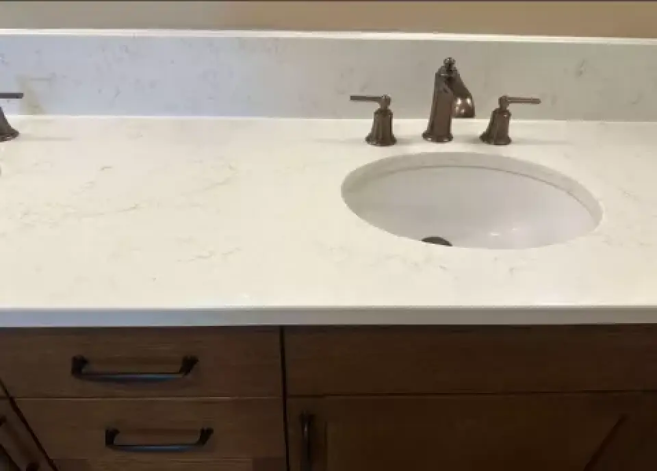 Bathroom sink with marble countertop and wooden cabinets. Bronze faucet with two handles.