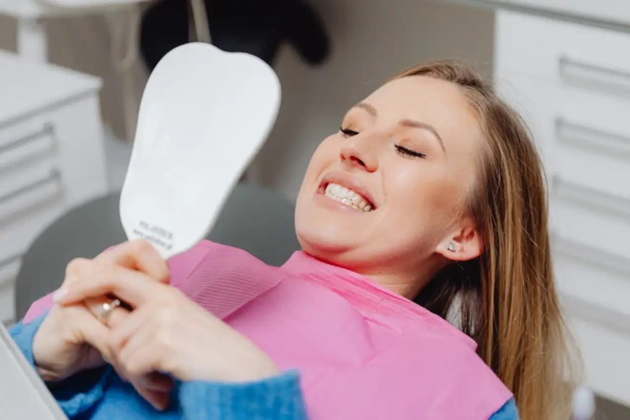 Woman smiling and looking at her reflection in a hand mirror at the dentists office.