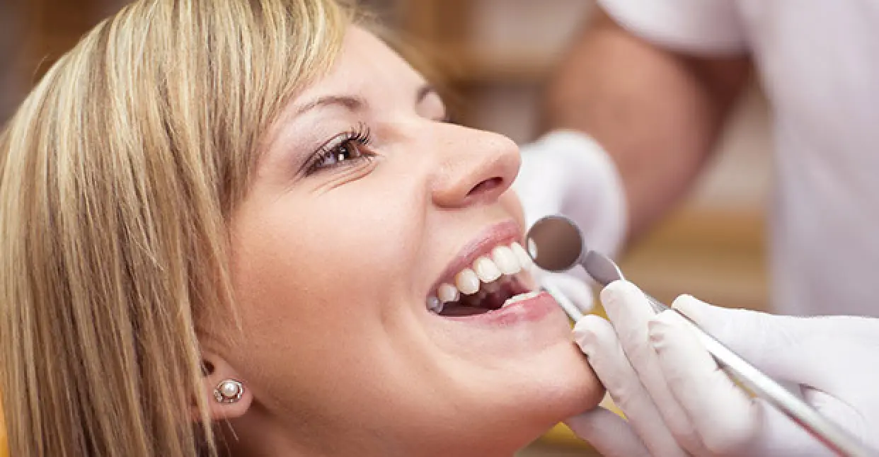dental worker viewing a womans teeth with mirror tool