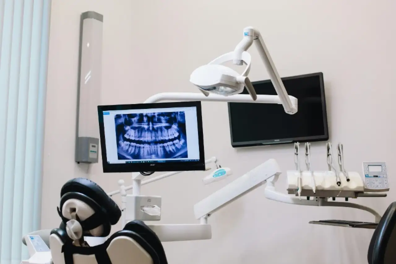 A dental office with a chair, x-ray on a monitor, and dental equipment nearby.