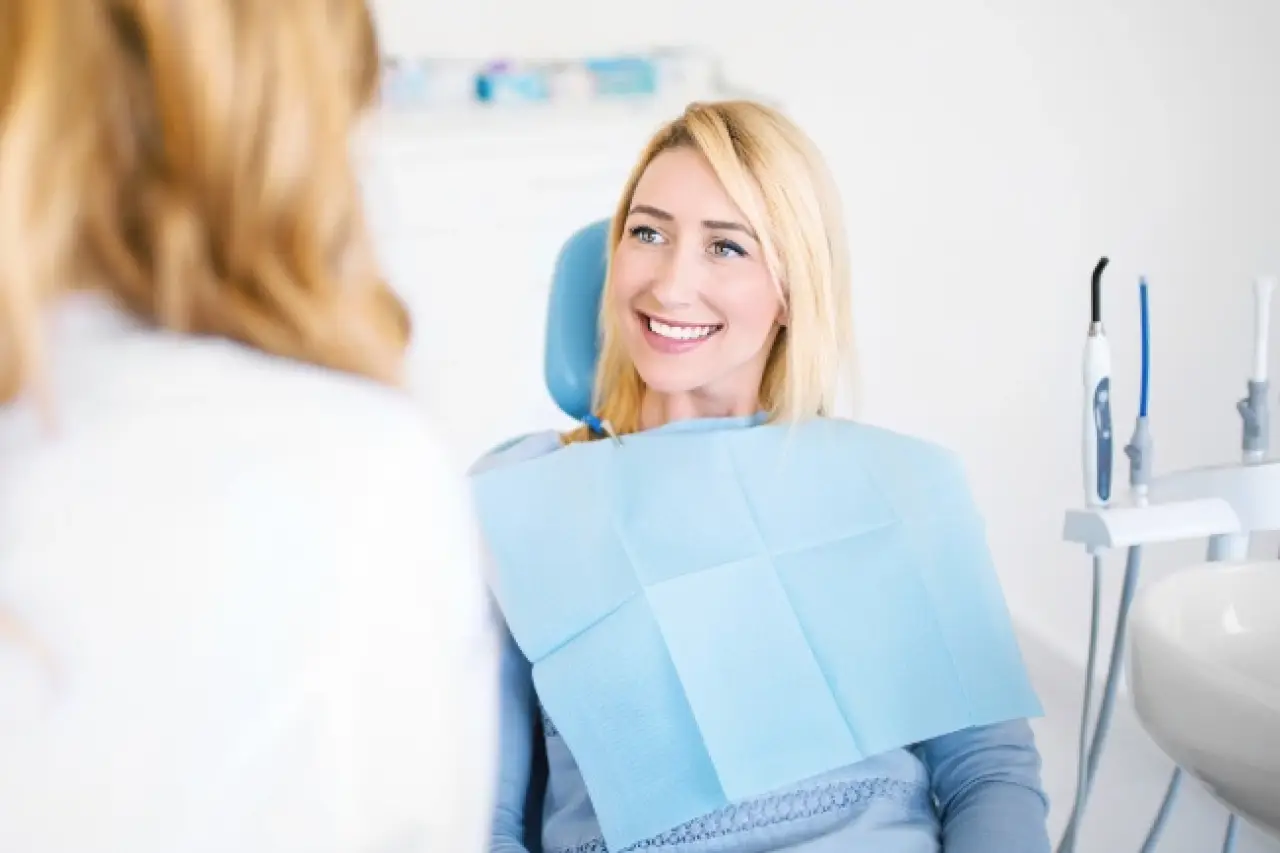 Smiling woman sitting in a dental chair, talking to a dentist in a bright clinic.