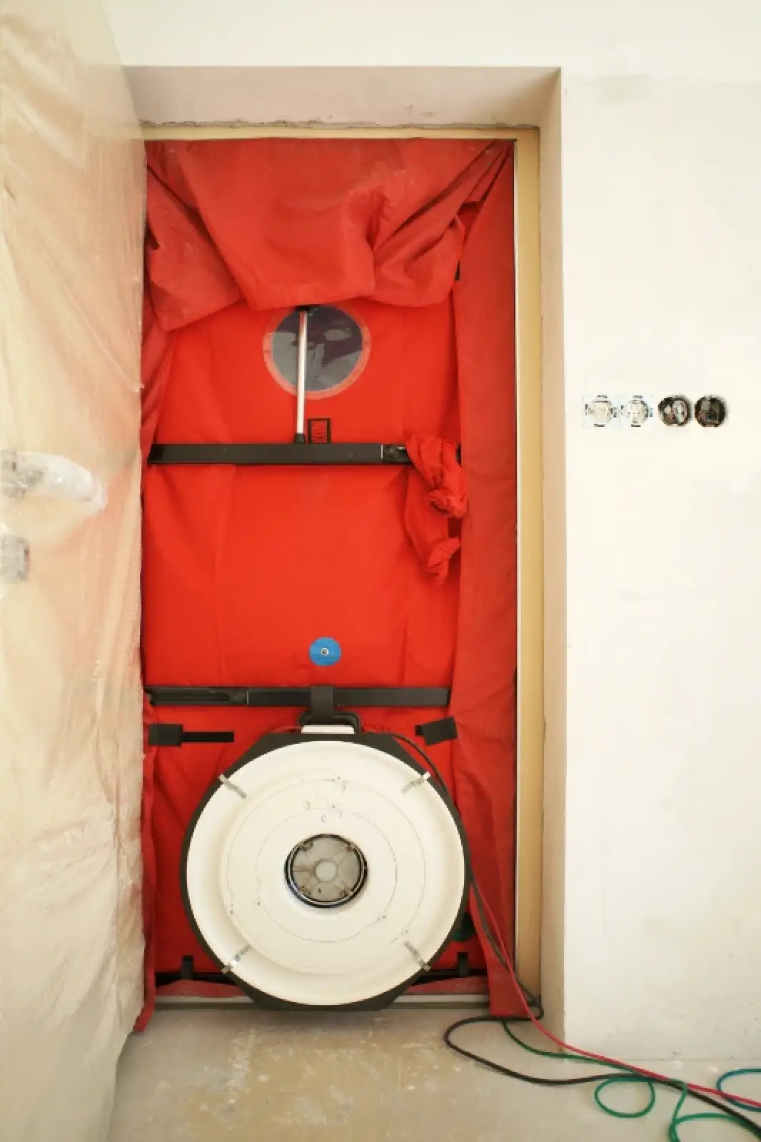 A blower door test setup in a doorway with red fabric and a large circular fan at the bottom.