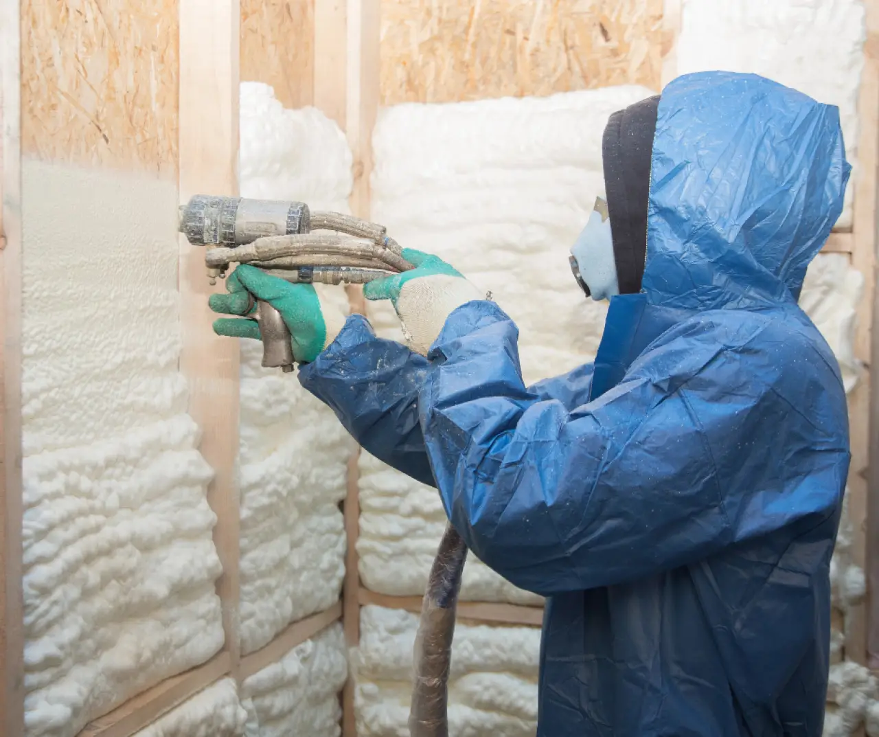 person in blue hazmat suit spraying insulation