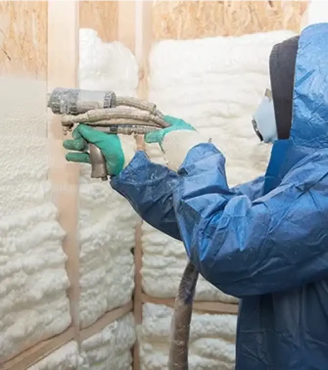 person in protective gear spraying foam insulation onto a wall