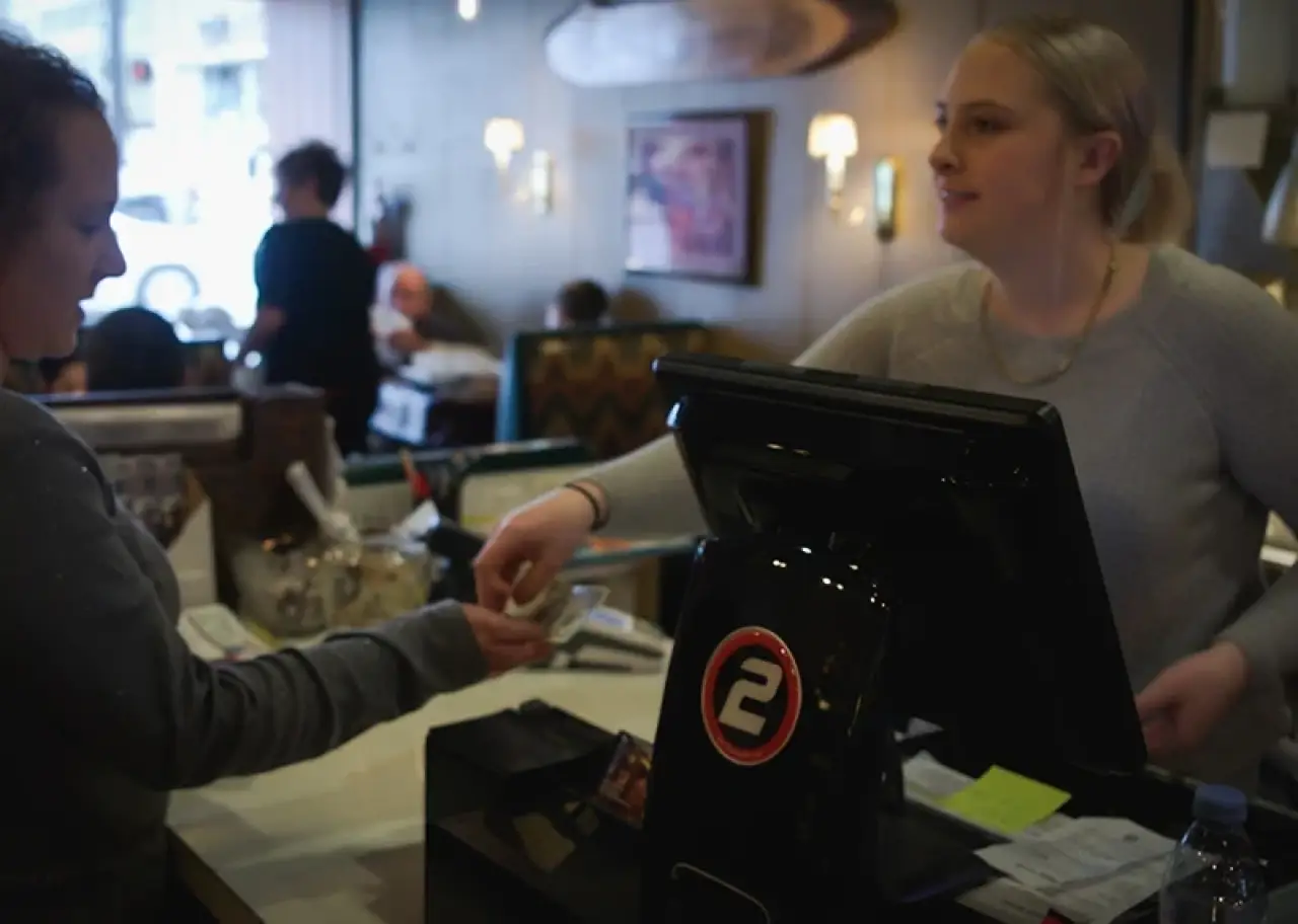 A cashier hands change to a customer at a restaurant counter with a register in front.