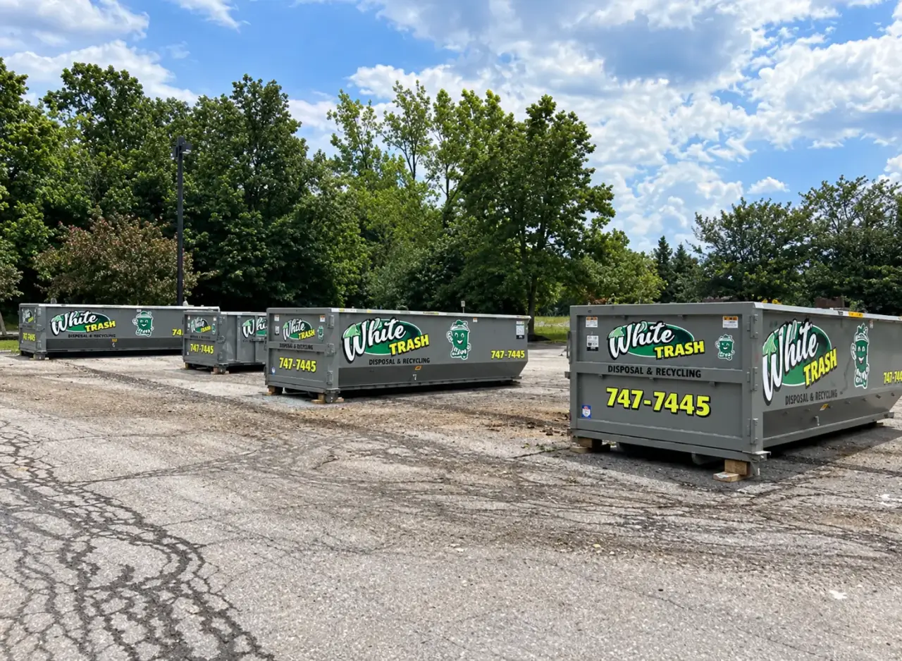 Four grey White Trash Disposal Recycling dumpsters in a parking lot.